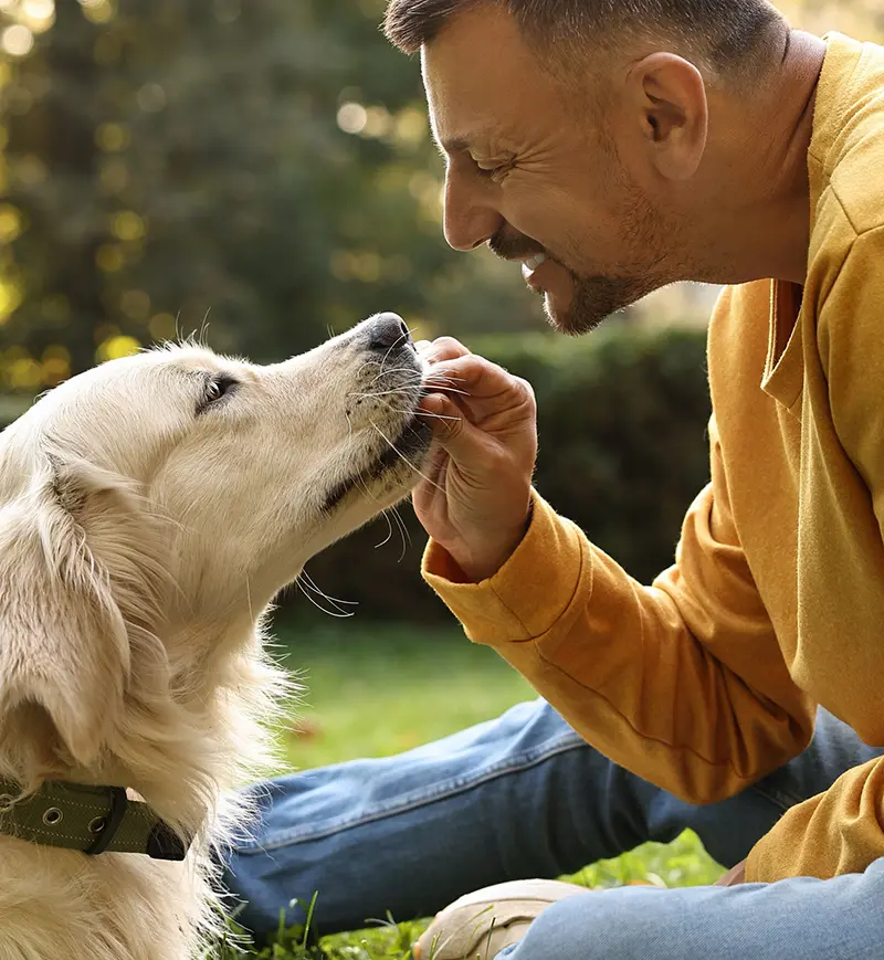 A man smiling and bonding with his golden retriever in a natural setting, highlighting pet-friendly living in Cascade Communities.